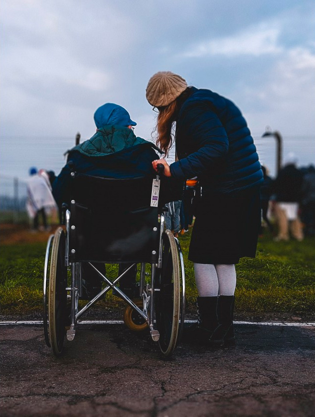 Person in a cheelchair with their back to the camera speaks to their friend standing next to them