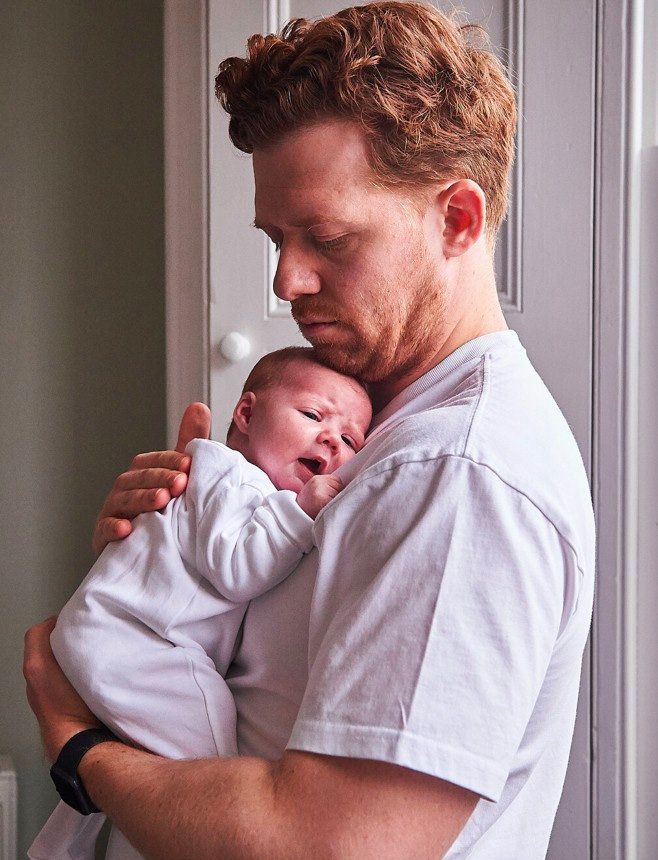 A white man holds a newborn baby to his chest