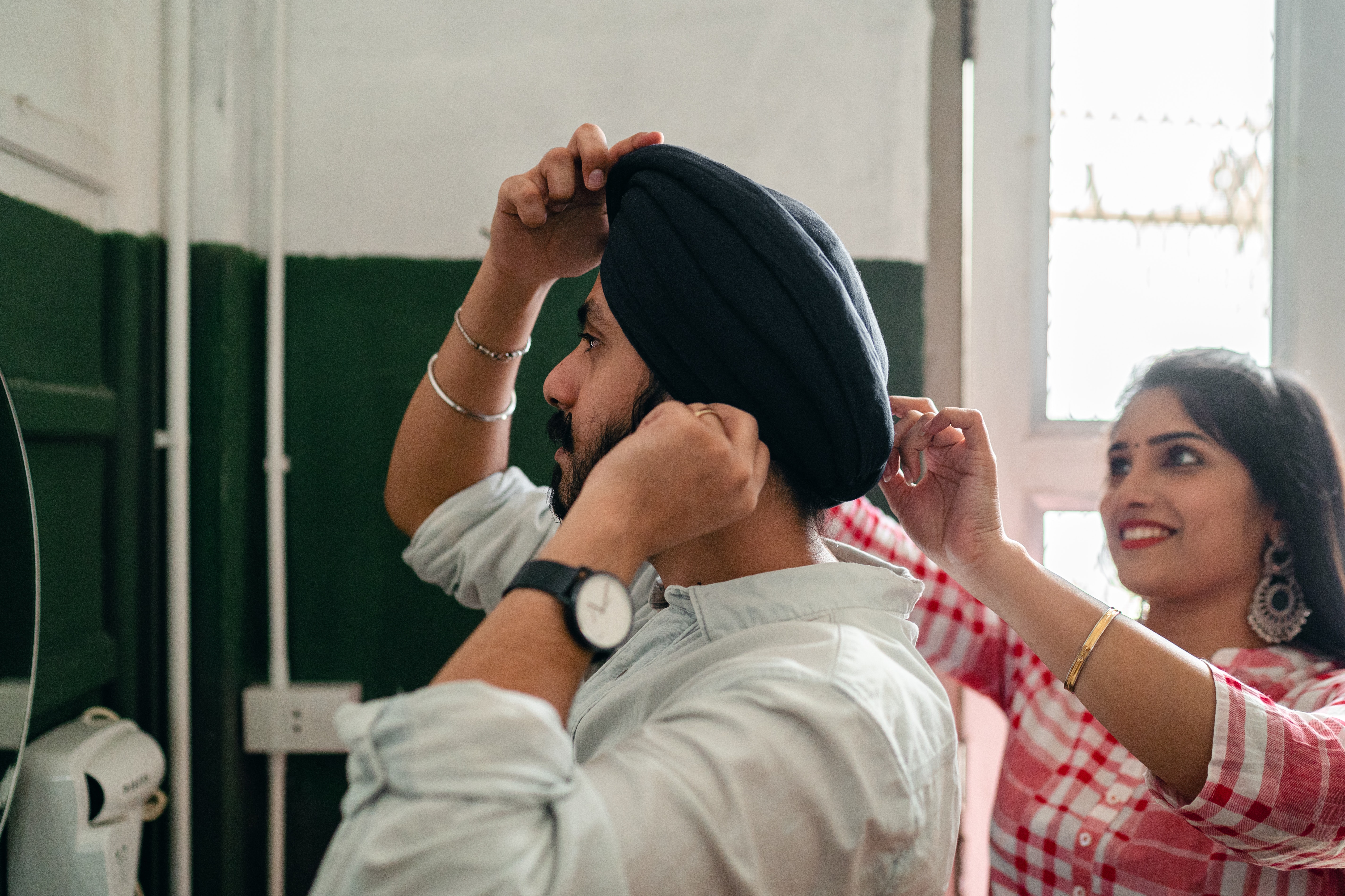 A woman helps her partner adjust his turban