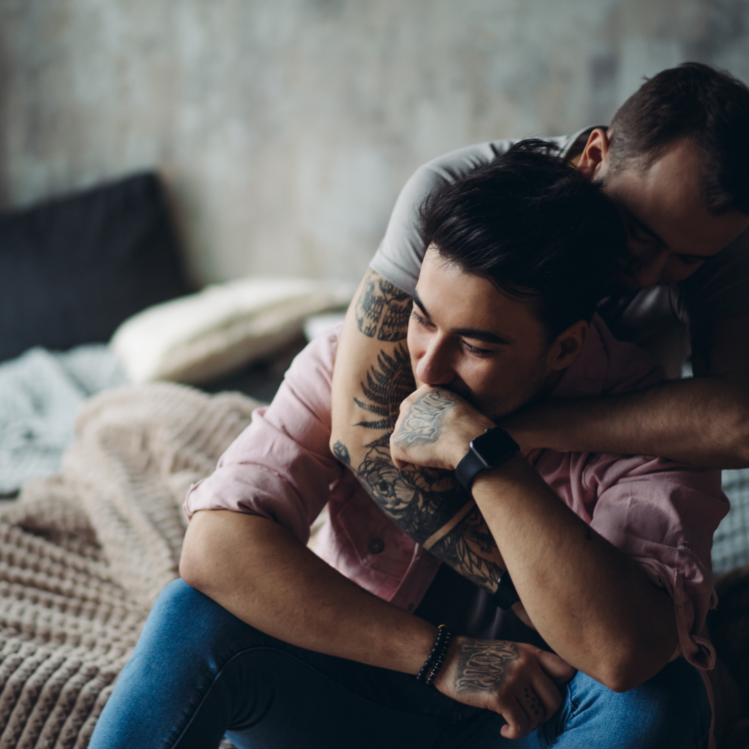 A smiling man being hugged by his male partner