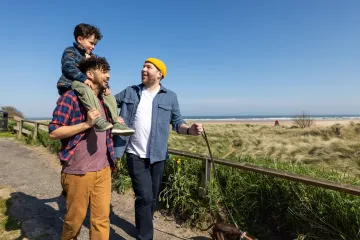 Two men walking outdoors, one carrying their toddler son on his shoulders